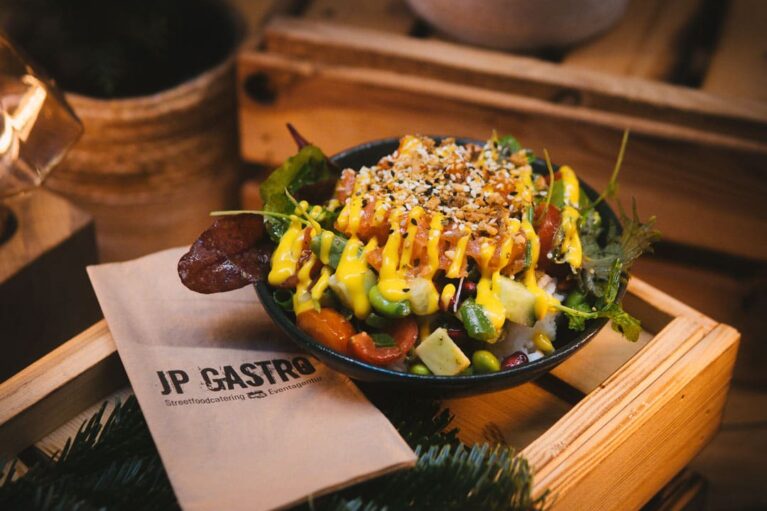 Eine frisch zubereitete Poke Bowl in einer Schale, die auf einer kleinen Holzkiste steht. Daneben liegt eine Serviete von JP Gastro