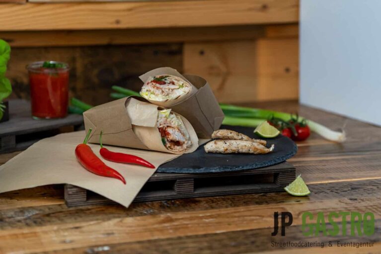 Zwei Hähnchenwraps, die mit Chilischoten, Hähnchenfleischstücken und Limetten auf einem schwarzen Schieferteller an einem Stand drappiert sind