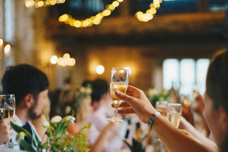 Mehrere Menschen sitzen an einem dekoriertem Tisch und erheben das Sektglas