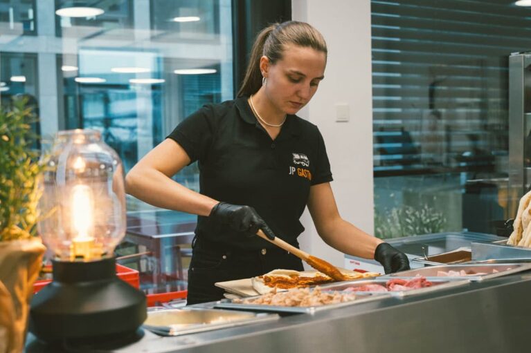 Eine Mitarbeiterin an einer Live-Cooking-Station, die Pizzen mit Tomatensauce bestreicht