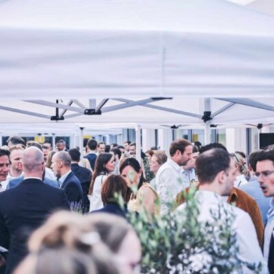 Größere Gruppe Menschen in Business-Kleidung unter weißen Pavillons während eines Firmen-Events
