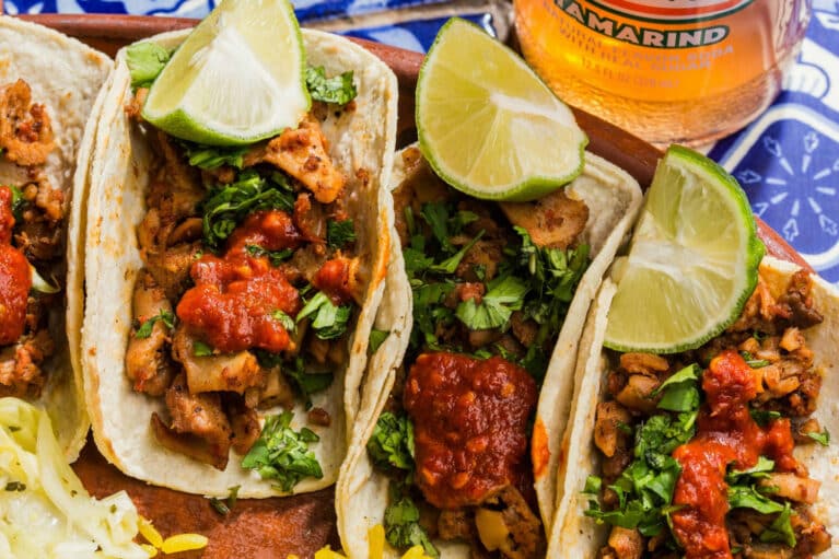 Tacos, die auf einem Teller mit einer Limette angerichtet sind.
